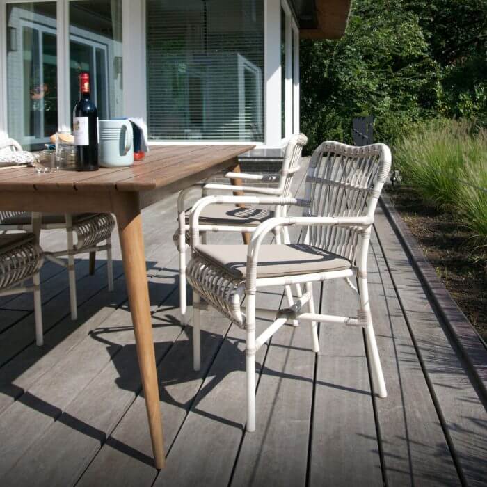 An inviting outdoor dining scene with a wooden table adorned with two wine glasses, surrounded by four white chairs on a wooden deck.