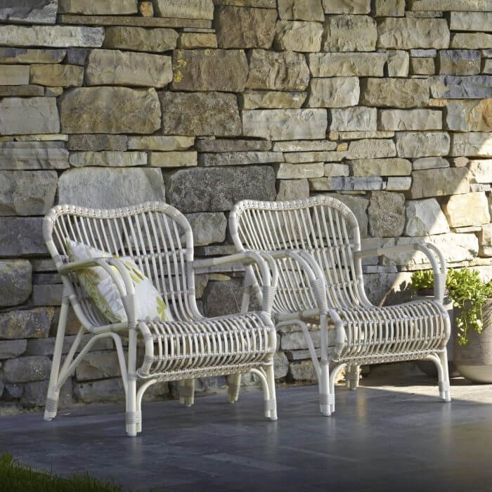 A charming outdoor seating arrangement with two outdoor white wicker chairs on a well-maintained patio, perfect for leisurely conversations.