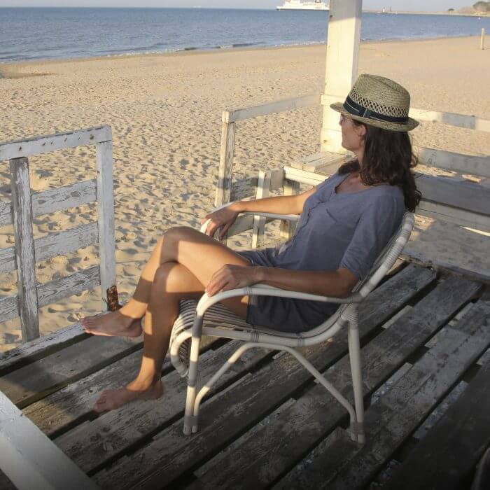 A serene waterfront scene with a woman in a gray dress sitting on a white outdoor lounge chair, enjoying a moment of relaxation by the water.