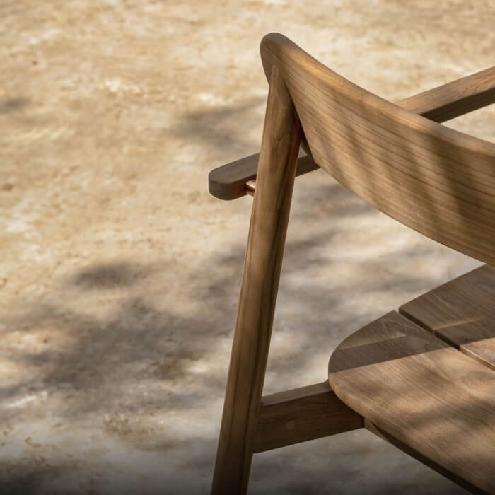 Teak outdoor chair with brass details, set in a serene natural environment